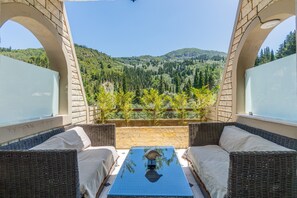 Un balcon agrémenté de meubles en osier, d’une table en verre et offrant une vue sur une colline boisée.