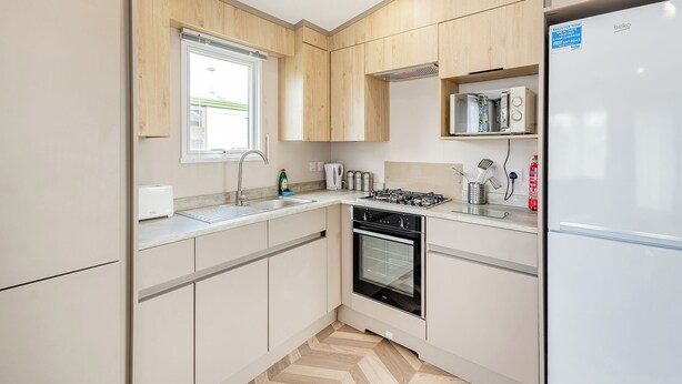 Een moderne keuken met houten kastjes, een inbouwoven, een gasfornuis en een koelkast.