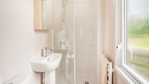 Een badkamer met een douche met glazen wand, een witte wastafel en een raam met uitzicht op groen.