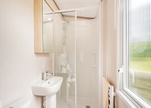 A bathroom with a glass-enclosed shower, a white sink, and a window with a view of greenery. - 2 bedroom accommodation in Kirkcudbright (Kirkcudbright)
