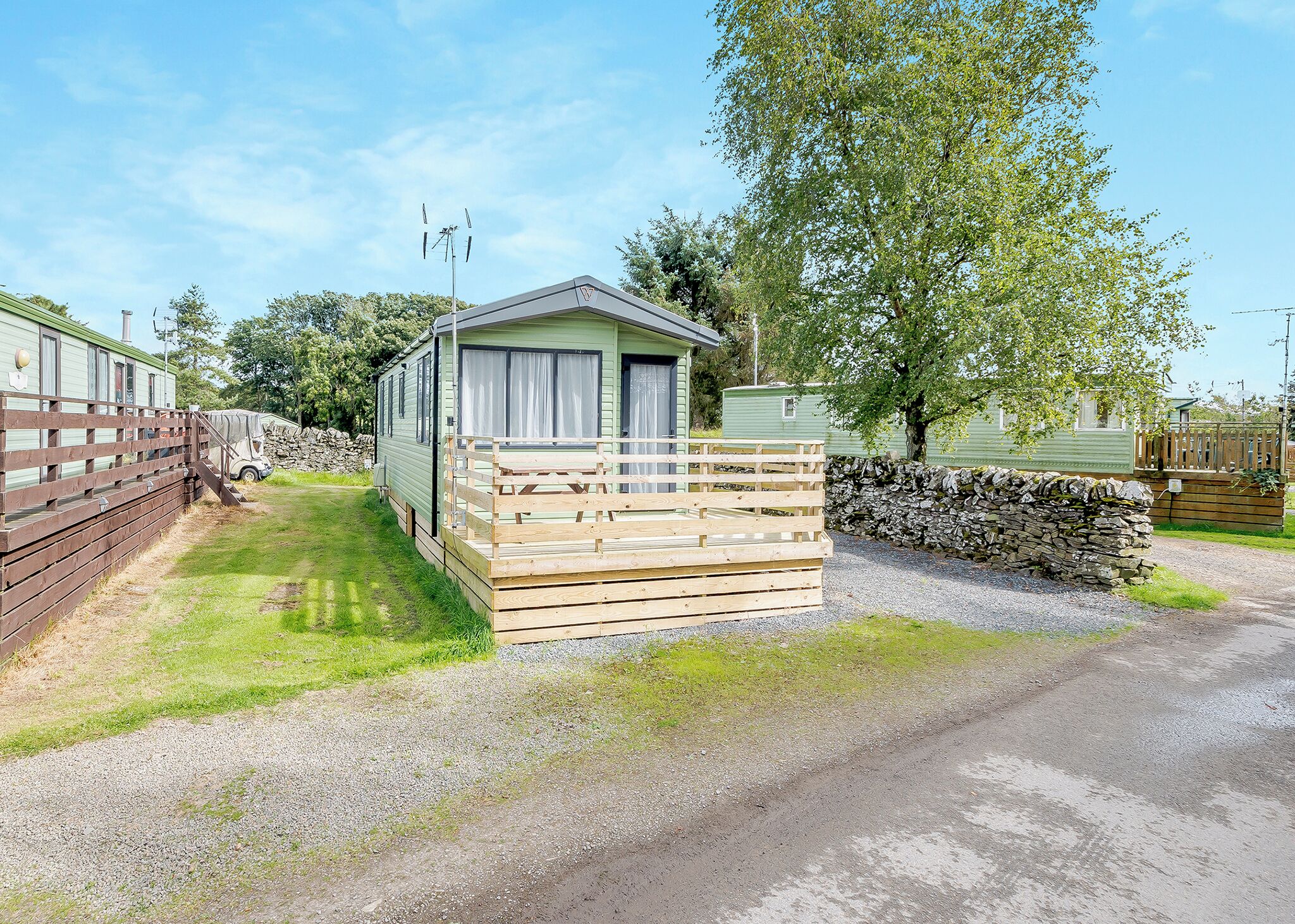 A caravan with a wooden deck and a stone wall.