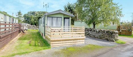 A caravan with a wooden deck and a stone wall.