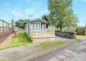 A caravan with a wooden deck and a stone wall. - 2 bedroom accommodation in Kirkcudbright (Kirkcudbright)
