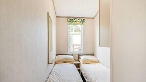 Een kleine, smalle kamer met twee eenpersoonsbedden, een raam met uitzicht en een spiegel aan de linkerkant.