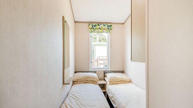 A small, narrow room with two single beds, a window with a view of the outside, and a mirror on the left wall. - 1 bedroom accommodation in Kirkcudbright (Kirkcudbright)
