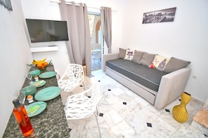 A compact living space with a sofa, dining table, chairs, a TV, and a cityscape picture.