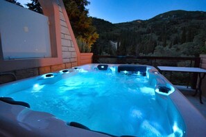 A hot tub with multiple jets, surrounded by a stone wall and a table, set against a mountainous backdrop.