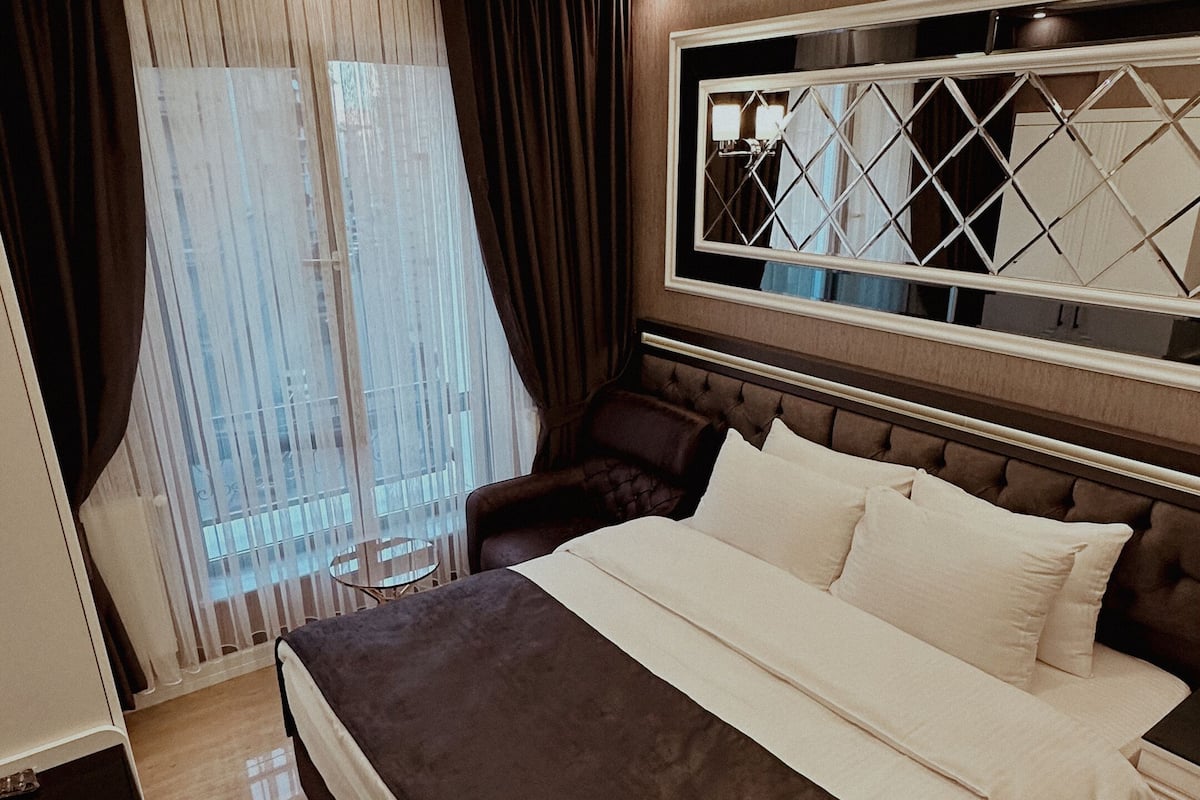 A modern hotel room with a large bed, a nightstand, a desk, and a window with curtains.