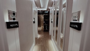 Ein Hotelkorridor mit Spiegelwänden, nummerierten Türen und einer modernen Leuchte.