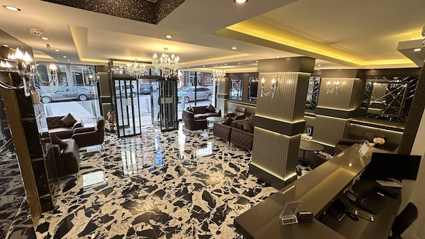 Eine moderne Hotelhalle mit Marmorboden, Ledersitzmöglichkeiten, einer Rezeption und einem Kronleuchter.