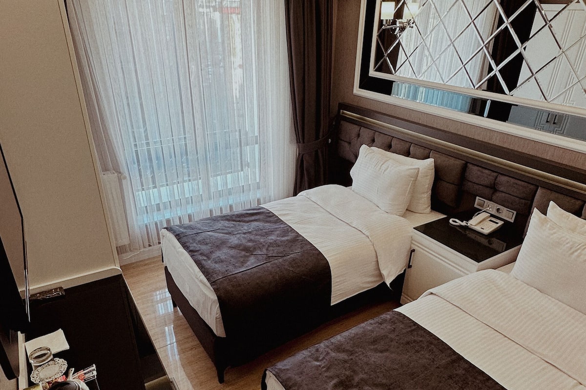 A hotel room with two beds, a desk, a mirror, and a window with curtains.