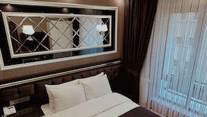 Ein modernes Hotelzimmer mit einem großen Bett, einem Nachttisch, einem Spiegel und Blick auf die Stadt durch das Fenster.