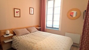 A bedroom with a bed, nightstands, a window with curtains, and wall decorations. - Appartement Proche Cathédrale (Albi)