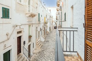 A narrow cobblestone street flanked by white buildings with balconies and green shutters. - Apartment 'Andreios' with Private Terrace, Wi-Fi and Air Conditioning (Ostuni)