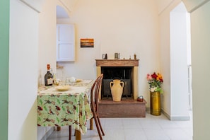 Un coin repas avec une table dressée pour deux personnes, une cheminée et un vase de fleurs.