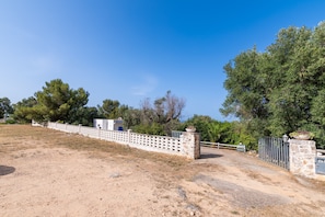 A fenced property with a dirt path leading to a building, surrounded by trees and greenery.