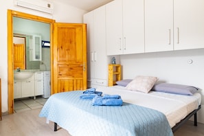 A bedroom with a bed, a wooden wardrobe, a bathroom with a mirror, and a sink.