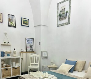 Une chambre à coucher comprenant un lit, une chaise, une petite table, une étagère avec des objets et un mur orné de tableaux encadrés.