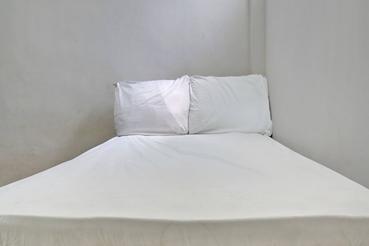 Ein kleines Zimmer mit einem Einzelbett, einer schlichten weißen Wand und einem schlichten Kopfbrett.