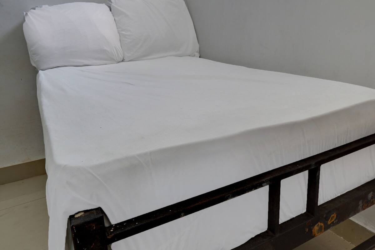 Ein Zimmer mit einem Einzelbett, einer weißen Matratze und einem schwarzen Metallgestell.