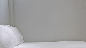 A single white bed in a room with plain white walls. - OYO Life 92919 Kost Wijaya Kusuma Lake Syariah (Madiun)
