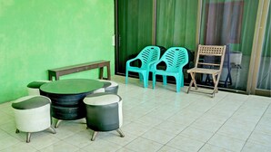 A small, tiled outdoor seating area with a round table and chairs, a bench, and a wooden chair. - OYO Life 92919 Kost Wijaya Kusuma Lake Syariah (Madiun)