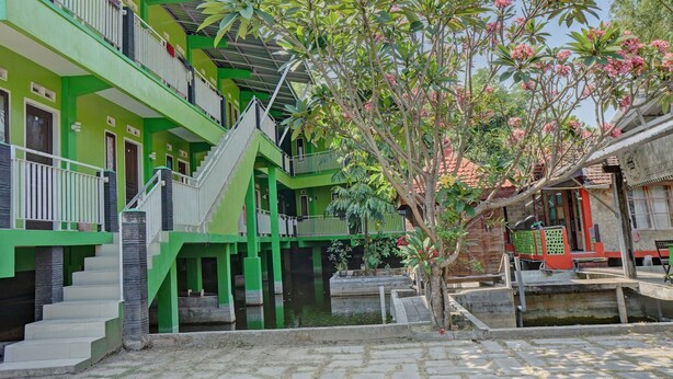 A multi-story building with green and white exterior walls, a staircase, and a small water feature in the courtyard. - OYO Life 92919 Kost Wijaya Kusuma Lake Syariah (Madiun)