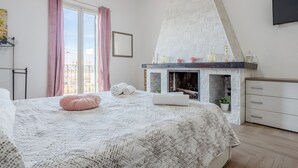 A bedroom with a bed, a fireplace, a balcony, and a TV mounted on the wall.