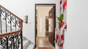 A staircase with a wooden handrail and black metal balusters, leading to a room with a wooden floor and a door with a floral curtain.