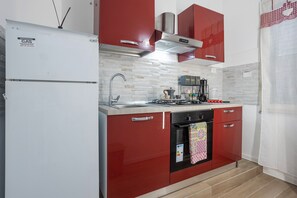 Une cuisine avec des armoires rouges, un réfrigérateur blanc, une cuisinière et un four à micro-ondes.