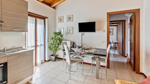 A modern kitchen with a dining area, wooden ceiling beams, a flat-screen TV, and a potted plant. - Apartment '38' with Shared Terrace and Balcony (Valeggio sul Mincio)
