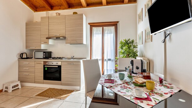 A compact kitchen with modern appliances, a dining table with a floral tablecloth, and a television mounted on the wall. - Apartment '38' with Shared Terrace and Balcony (Valeggio sul Mincio)