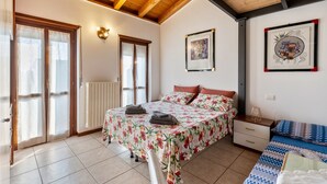 A bedroom with a bed, a nightstand, a window with curtains, a radiator, and a ceiling with wooden beams. - Apartment '38' with Shared Terrace and Balcony (Valeggio sul Mincio)
