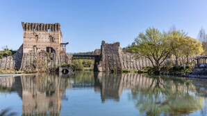 A historic stone structure with a bridge over a calm body of water, surrounded by trees. - Apartment '38' with Shared Terrace and Balcony (Valeggio sul Mincio)