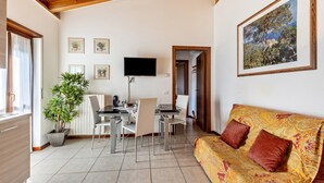 A room with a dining area, a sofa, a TV, and a painting on the wall. - Apartment '38' with Shared Terrace and Balcony (Valeggio sul Mincio)