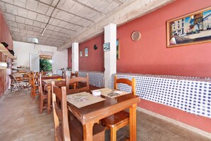 A restaurant with wooden tables and chairs, a red wall with a painting, and a checkered tablecloth.