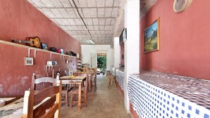 A narrow corridor with wooden chairs and tables, a guitar on a shelf, and a tiled counter.