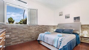 A bedroom with a bed, a nightstand, a window, and a wall with a textured pattern.