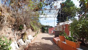 Une ruelle étroite, avec une rangée de bancs blancs sur le côté gauche, des plantes en pot sur le côté droit et un bâtiment rouge en arrière-plan.
