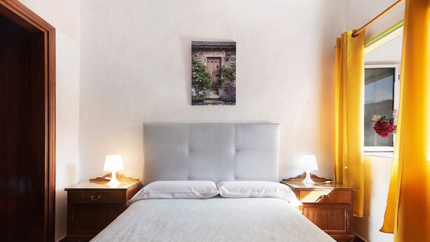 Une chambre à coucher avec un lit, deux tables de chevet avec des lampes, une tête de lit, un tableau encadré au mur et une fenêtre avec des rideaux.