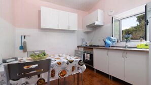 Une cuisine avec des meubles blancs, une fenêtre donnant sur un beau paysage et une table recouverte d’une nappe.