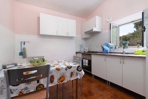 Une cuisine avec des meubles blancs, une fenêtre donnant sur un beau paysage et une table recouverte d’une nappe.