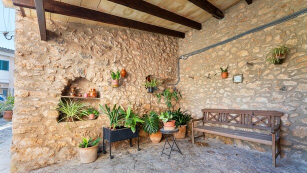 Un mur de pierre agrémenté de plantes en pot, un banc et un plafond en bois rustique.