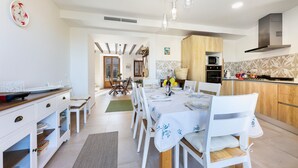 Une cuisine moderne avec des meubles blancs, un coin repas avec des chaises blanches et une horloge visible au mur.