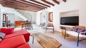 Un salon moderne avec un plafond en bois, des canapés rouges, une table basse en bois, des fauteuils en osier, un téléviseur et un escalier menant à une autre pièce.