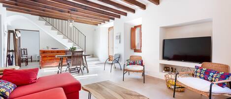 Ein modernes Wohnzimmer mit Holzboden, roten Sofas, einem Holztisch, Korbstühlen, einem Fernseher und einer Treppe, die in einen anderen Raum führt.