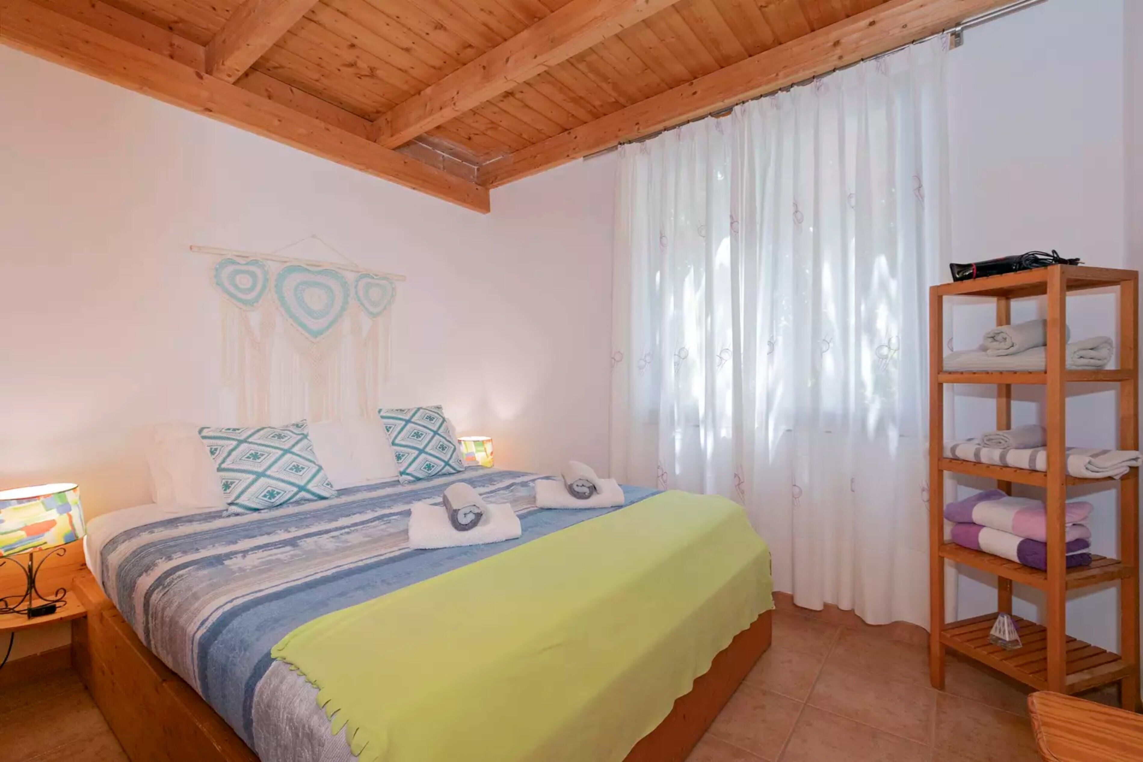A bedroom with a bed, a wooden headboard, a shelf with towels, and a lamp.