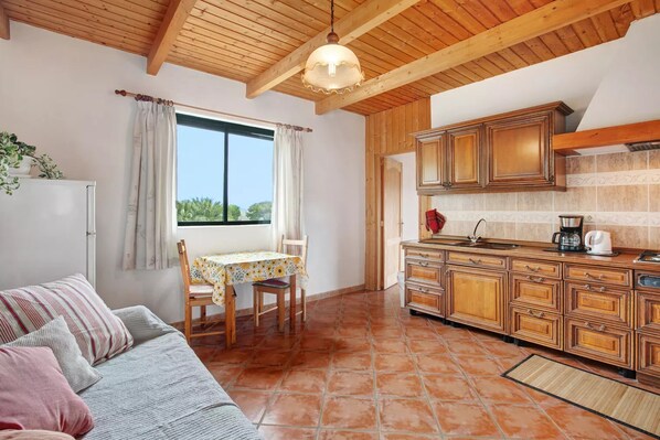 A kitchen with wooden cabinets, a dining table with chairs, a refrigerator, and a window with curtains.
