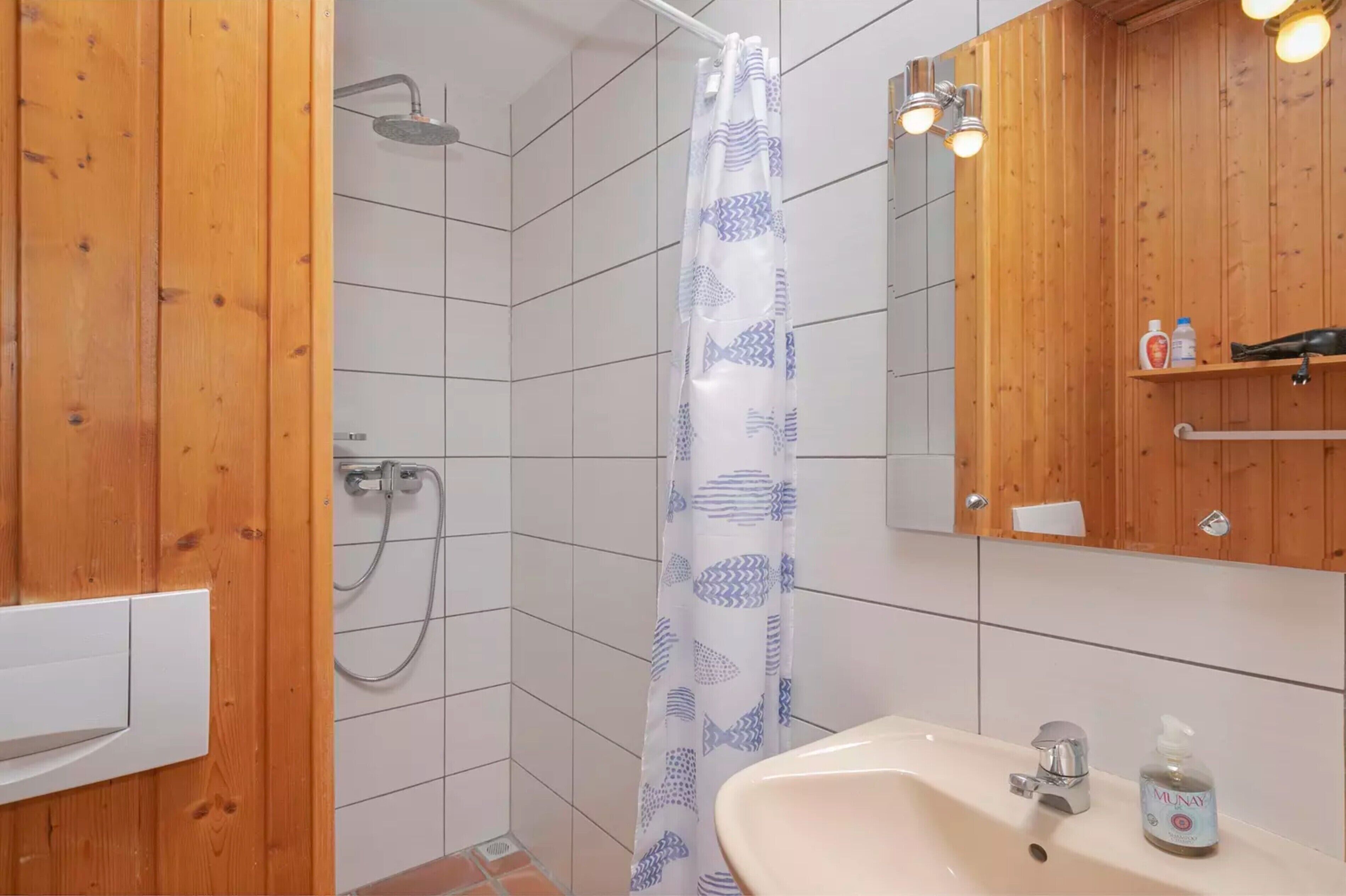 A bathroom with a shower, a sink with a mirror, and wooden walls.