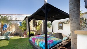 Una cama con dosel colorido, una pared de piedra y una bicicleta al fondo.